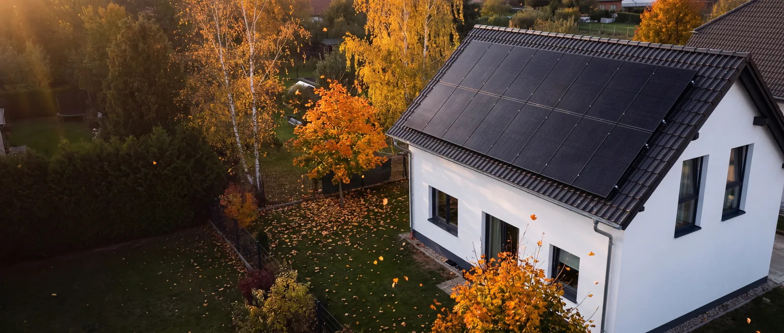Rodinný dům s celočernými fotovoltaickými panely na střeše, podzimní zahrada