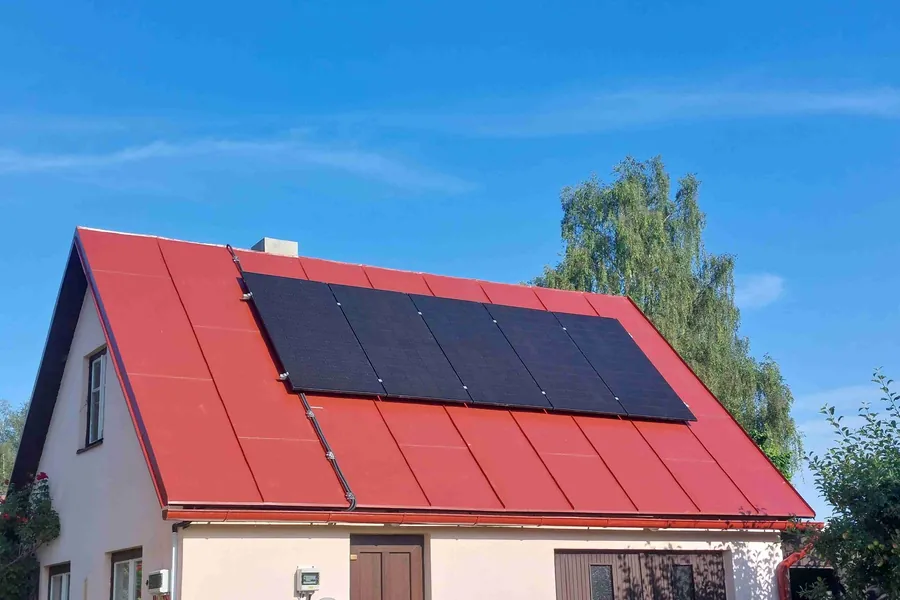 Dům ve Svratouchu s červenou plechovou střechou a celočernými panely