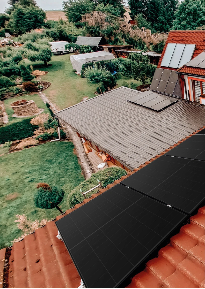 Tři zasklené solární kolektory na červené taškové střeše a pod nimi pole tmavých fotovoltaických panelů na stejném domě
